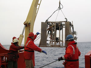 Marine Technician Jamee Johnson (left) and WHOI Research Associate Erich Horgan hold guide lines while Eric Hutt uses hand signals to guide the winch operator, as LAPIS is lowered over the side of the Gould. (Photo by Kelly Rakow, WHOI)