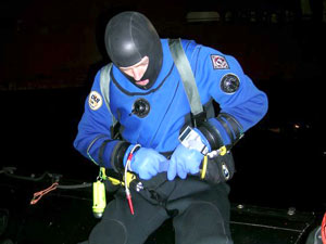 Still in the light of the ship, Byron Pedler begins to get ready to dive, buckling on his weight belt.