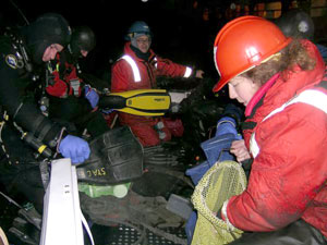 Wally, at the open cooler, loads a diver&rsquo;s collecting bag with jars, which must be full of water when taken down, so that the increased pressure won&rsquo;t seal them too tightly to open.