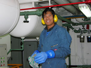 Oiler Roberto Cortes, wearing traditional ear protectors, cleans pipes in the spotless engine room of the Gould. 