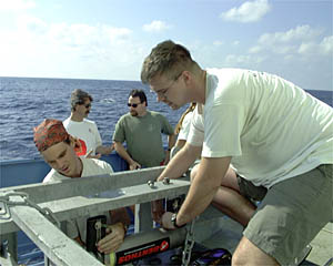 Greg Kurras (left) and Del Bohnenstiehl (right) work on the Towed Camera Sled while Paul Oberlander and John Cawley talk by the railing. 