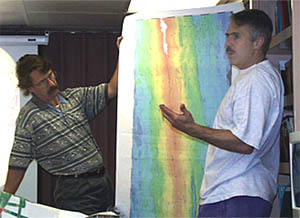 Dan Fornari discusses his research on the geology and hydrothermal processes at the East Pacific Rise. Paul Oberlander helps to hold up a multibeam bathymetric map that shows the detailed seafloor topography, or bathymetry, of the ridge in the 9-10°N area.