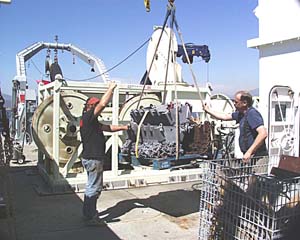 Ron Comer and Will Sellers, of Woods Hole Oceanographic’s (WHOI) Deep Submergence Group, help guide rock dredges onto the ship.
