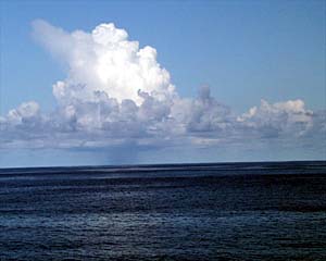 Clouds over the tropical ocean can be spectacular. This afternoon we saw lots of white puffy cumulus clouds, some with local rain squalls under them. If you look carefully you can see the vertical band of gray-blue extending down from the tall part of the cloud which is where it is raining. 