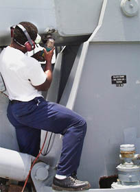 Cletus Fennell, one of Melville’s Ordinary Seamen, grinds away rust spots on the aft crane in preparation for painting. 