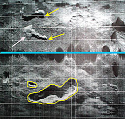 A DSL-120 sonar record from the 1&deg; 40’-50’N area of the East Pacific Rise crest collected today. The yellow arrows point to fissures or cracks in the volcanic seafloor that are likely places for lava to erupt. The pink arrow points to a small lava flow that appears to have covered up part of the fissure and may have erupted from it. Yellow lines are drawn around two “collapse features”. The larger one may be a “lava lake” - a place where lava erupted and formed a small lake, but later it drained back into the underlying crust, leaving a large pit in the seafloor. All these places are likely to have young lava flows. The blue line in the middle of the record is the nadir -- the track of the DSL-120 “sonar” fish. The horizontal white lines are spaced 100 meters apart. 