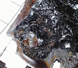 A close-up of a fresh, glassy basalt exterior. The rocks dredged today are some of the youngest ones seen on this expedition. Some of the glass has an iridescent surface -- a characteristic of newly erupted seafloor lava. The bold scale lines at the upper left corner are 1 centimeter apart.