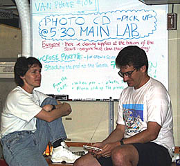 Maya Tolstoy and Dan Scheirer chat in the Main Lab after dinner. Plans for the post-cruise party on Wednesday night and notices about the cruise CD and T-shirts are posted on the white board behind them.