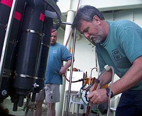 Researcher Eric Olson draws water samples moments after the CTD arrives on the deck. Scientists on the ship trigger the large gray bottles (labeled here with pink numbers) to trap water at various depths to measure changes in the water chemistry.  