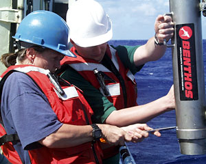 Geochemist Susan Humphris and Chemist Darryl Green remove the “pinger” from the wire after completing the rock dredge is complete. The “pinger” is placed above the rock dredge. It simultaneously bounces a sound signal off the sea floor and directly back to the ship. That helps scientists determine the location of the rock dredge above the seafloor.  