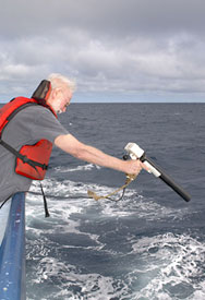 Dan Jacobsen, the computer tech, deploys an XBT (eXpendable BathyThermograph). This instrument consists of two copper wires (1000m long) attached to a torpedo shaped weight. The weight drops into the water from the gun Dan is holding with the copper wires streaming behind. The weight contains a temperature sensor and electronics that measure the temperature. The temperature is then sent through the copper wires back to the ship and recorded. These data are used to make a temperature versus depth profile and serve to calibrate the sound velocity tables of the multibeam sonar.  