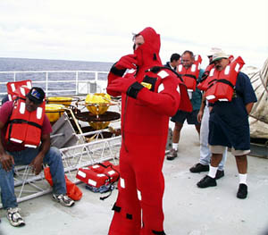 James Pearson, Able Seaman, demonstrates how to put on a ‘Gumby’ survival suit during today’s drill. This suit provides both insulation and floatation should it become necessary to abandon ship.  