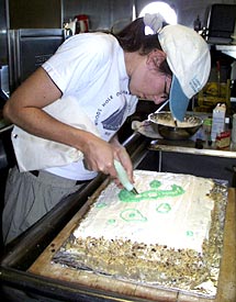  Christy Reed helps ice Dan Fornari’s birthday cake. The decorations are in the shapes of the Gal&aacute;pagos Islands. Christy is making Isabela in the photo. 