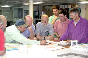 Scientists study a bathymetric map to discuss the plans for operations at the Rose Garden hydrothermal vent site. From left to right: Bob Collier, Dana Yoerger, Tim Shank, Al Bradley, Dan Scheirer, Steve Hammond and Dan Fornari.
