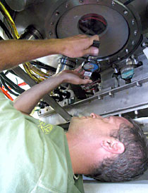 Alvin Technician Gavin Eppard, on his back under Alvin. He had squeezed into a 6-inch space to examine the vessel's underside window. This is one of the many regular maintenance checks performed on the sub. In this case, Eppard determined that the window did not need replacing. 