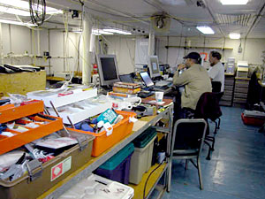 he ABE lab on board R/V Atlantis, with Dana Yoerger and Al Duester at the controls. Other ABE Group members on board this cruise are Rod Catanach and Cindy Sellers. This is where ABE is programmed before diving, monitored as it dives, and downloaded once it arrives back on board. The data ABE brings back is analyzed here as well, as a first step toward creating the high-resolution maps that will aid further research. The toolboxes visible here are just part of the backup; everything from spare parts to an entire spare computer live in this lab. 