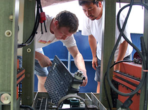 Volcanologist Adam Soule (left) and biologist Walter Cho attach instruments for use on the towed digital camera system during night operations.