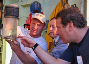 WHOI guest Dan Dubno points to a white crab captured at Rosebud using Alvin. Scientists Tim Shank (in hat) and Susan Humphris explain it is a scavenger that can grow to about the size of a hockey puck. (Photo by Amy Nevala)