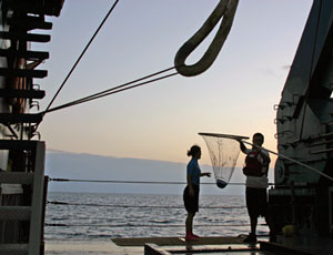 Seaman Robert Barrett (with net) and shipboard computer technician Kazumi Baba retrieve a hardhat dropped overboard during Alvin�s recovery (Photo by Amy Nevala)