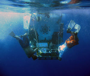 Swimmers Carl Wood (left) and Ken Feldman unhook the safety lines that provide support to the basket on Alvin as it enters the water. Divers use the basket to store animals, rocks and other samples collected from the seafloor. (Photo by Mark Spear)