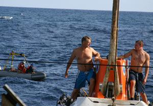 Swimmers Carl Wood (left) and Anthony Berry stand on top of Alvin as it is lowered to the sea during deployment. Behind them is the recovery boat. (Photo by Amy Nevala)