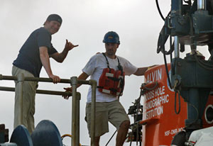 Before climbing into Alvin, volcanologist Adam Soule signals �hang loose� to a small crowd on the ship�s deck. He is part of today�s team making this expedition�s final dive to the seafloor. Pilot in training Anthony Berry helps him inside the submersible. (Photo by Amy Nevala)