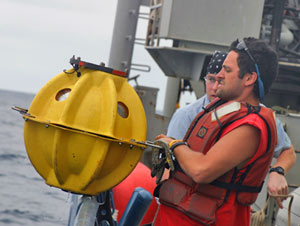 2. Seamen Rob Barrett and Mike Mulkern haul a transponder on board after its release from the seafloor. During our time at sea, Alvin divers used it for navigating the seafloor. The transponder is housed inside the protective plastic sphere. (Photo by Amy Nevala)
