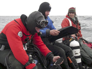 At the dive site, Jeff Mercer gets ready to lift his air tank while Sandy Williams puts on his fins. Marine Technician Jamee Johnson holds Sandy�s tank. (Photo L. Madin, WHOI)