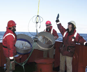 During a daytime plankton tow, L. M. Gould Marine Technician Jamee Johnson and WHOI engineering assistant Josh Eaton (blue hard hat) stabilize MOCNESS as the winch lifts it over the stern.