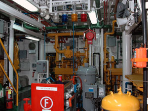 The engine room of the L. M. Gould is white, well-lit, and has all sizes of pipes, painted bright colors, running throughout the room: blue for fresh water, green for seawater, yellow for fuel, and so on.