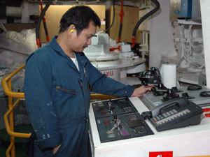 Assistant Engineer Noli Tamayo, wearing nearly-invisible ear plugs for noise protection, at the emergency control console, next to the white rudder cap. Some of the ship’s 700 miles (1,126 kilometers) of electrical wiring, painted white, are on the wall to the right.