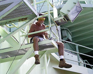 Ken Kenerson chipping rust and painting the catwalk railings on the 01 deck, starboard side. Keeping the ship painted and free of rust is an important job done by members of the Deck Department. 