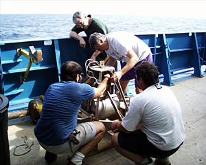 Dan, Jim, Jerry and Ed prepare the grab sampler for a quick trip to the seafloor. This device is designed to crash into the rocks on the seafloor and snap shut, thus "grabbing" a sample. After it has hit bottom, it is hauled back up to the deck of Atlantis.