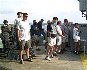 Scientists and ship's crew gather to welcome Gary and Bob back from their successful trip to the bottom. Margo and Del (standing in front of the capstan) carefully conceal one of the hoses that will be used to give the new Alvin divers their watery reward.