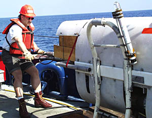 Craig Elder, a member of Woods Hole Oceanographic Institution’s Deep Submergence Operations Group, holds the tailend of the sonar fish. Because of its shape, this part is called the “lollipop.” You can see that Craig is wearing a hard hat and work vest. Safety is an important concern, especially when moving heavy equipment on a rolling platform like a ship on the ocean.