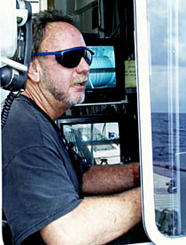 Rick Koppel, one of Melville’s oilers, stands the “winch watch” during dredging operations this afternoon. He has to operate the winch and let wire out or pull it in. There are 11,000 meters of steel wire on the large winch drum that is below deck. He uses the TV monitor that you see behind him to keep a close eye on the winch drum to make sure that the wire spools off correctly and doesn’t get tangled.