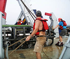 Tim Haskell (foreground), Ben Wigham (background), and Craig Elder help tend the safety lines as Argo II is hauled on board the fantail of R/V Melville.