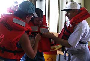 Safety training comes on the second morning of the expedition. Amy Simoneau (left) and Dan Fornari (right) help Jenney Hall adjust her lifejacket. The researchers practice rescue boat drills and learn the sounds of horn blasts for emergencies. The signal for abandon ship is seven short whistle blasts followed by a long blast.