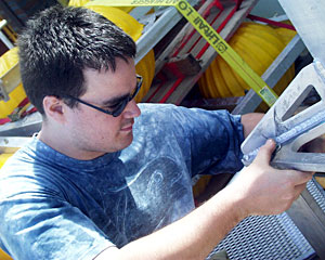 DSOG team member Mark Bokenfohr assembles the “elevator.” It functions like a regular elevator, but instead of hauling people it transports sampling equipment. The large yellow balls (in the background) provide flotation when scientists release the elevator from the sea floor.
