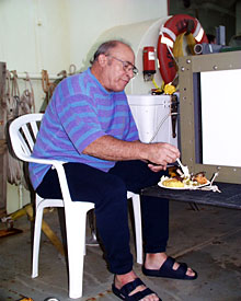 Second Assistant Engineer Paul “Skook” Lovejoy uses the elevator as his table during the cook-out.  