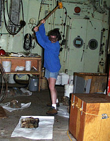 Graduate student Rachel Gallant slams a sledgehammer on a volcanic rock. Geologists Susan Humphris and Dan Fornari dredged several loads today, and each rock must be cut and described.  