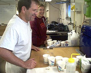 Mark Kurz and Kate Buckman process the rock core samples. The wax, with the glass chips embedded in it, is melted in a microwave in a cup of water. The water heats up, the wax melts and the glass bits fall to the bottom of the cup. After several heatings most of the wax is removed and the samples are ready to be bagged.