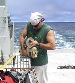 Steve Volpe wraps up the dredge weight in a burlap sack. The weight is placed in the bottom of the dredge to stop the chain bag from becoming twisted as it descends to the seafloor. It is wrapped in burlap so small pieces of volcanic glass get collected in it.