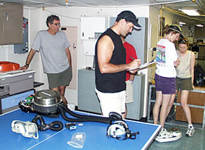 Anyone going down in Alvin has to be weighed so that the total payload of the submersible is known for every dive. Stace Beaulieu weighs herself while Bruce Strickrott keeps the records.