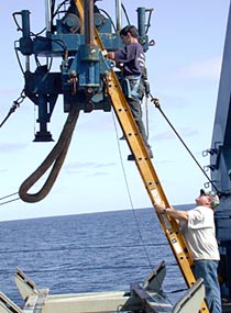 While Alvin is submerged, the ship’s crew conducts important routine maintenance. Oiler Mike Spruill (on ladder) and Third Engineer Phil Treadwell lubricate the A-frame that maneuvers Alvin in and out of the water.