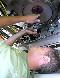 Alvin Technician Gavin Eppard, on his back under Alvin. He had squeezed into a 6-inch space to examine the vessel's underside window. This is one of the many regular maintenance checks performed on the sub. In this case, Eppard determined that the window did not need replacing.