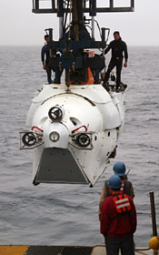 Despite misting rain and cold wind, eager observers collect on deck at 7:30 a.m. to watch the first Alvin dive of the expedition. Two swimmers standing on the sub—Mark Spear (right) and Raul Martinez—are certified to help deploy Alvin after it is lowered into the water.