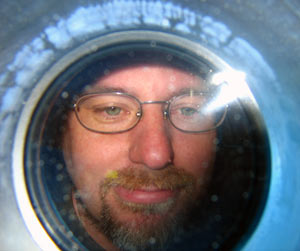 Anthropologist Stefan Helmreich of the Massachusetts Institute of Technology peers from a porthole during his first dive in Alvin. Swimmer Mark Spear dived underwater to capture the photo while helping to deploy the sub.