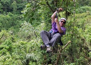 WHOI geologist Dan Fornari races from tree to tree on a zip line, a wire extending through an area of the Costa Rican jungle near Arenal Volcano. He uses a gloved hand to steady his body, and the same hand to pull on the wire to slow down.