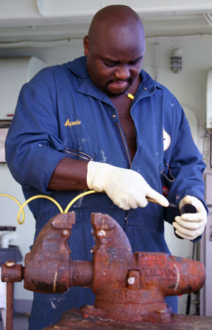 Oiler Charlie Apudo uses pressurized air to blast debris from sink drains. Charlie hails from Kenya and sometimes greets people with jambo, Swahili for “hello”.
